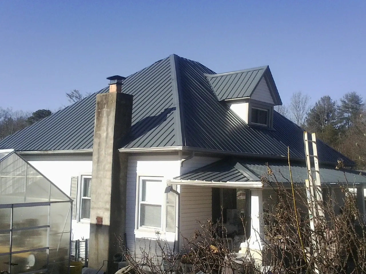 Dark blue standing seam metal roof on a white farmhouse with dormer — Slate & Tile Roof Repair by Roofing Brothers in Corral