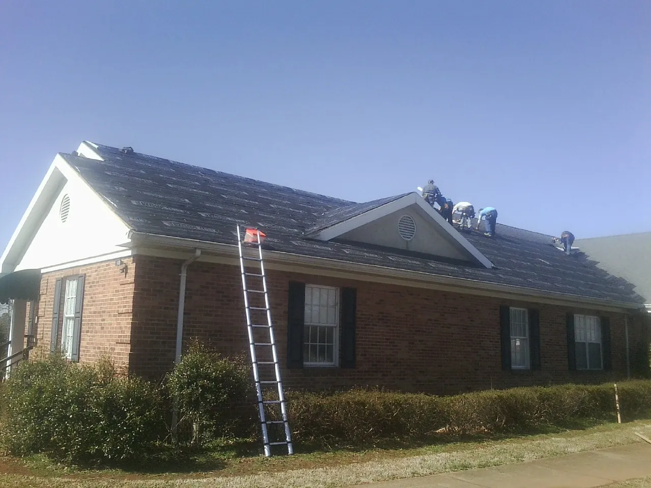 Crew tearing shingles off a brick ranch roof with a ladder set — Emergency Roof Repair work by our crew in Corral