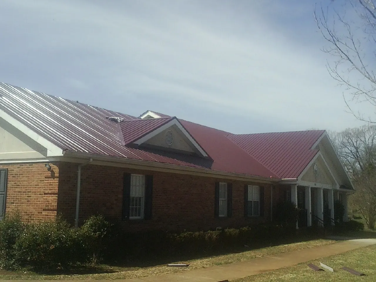 Red metal roof with gabled entries on a long brick building, from a Hail Damage Roof Repair job in Corral