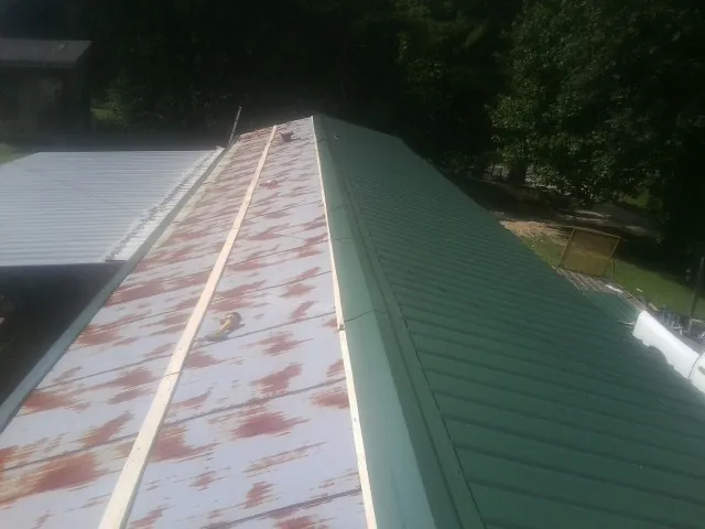 Old rusted panels beside newly installed green metal roofing — Wind Damage Roof Repair by Roofing Brothers in Corral