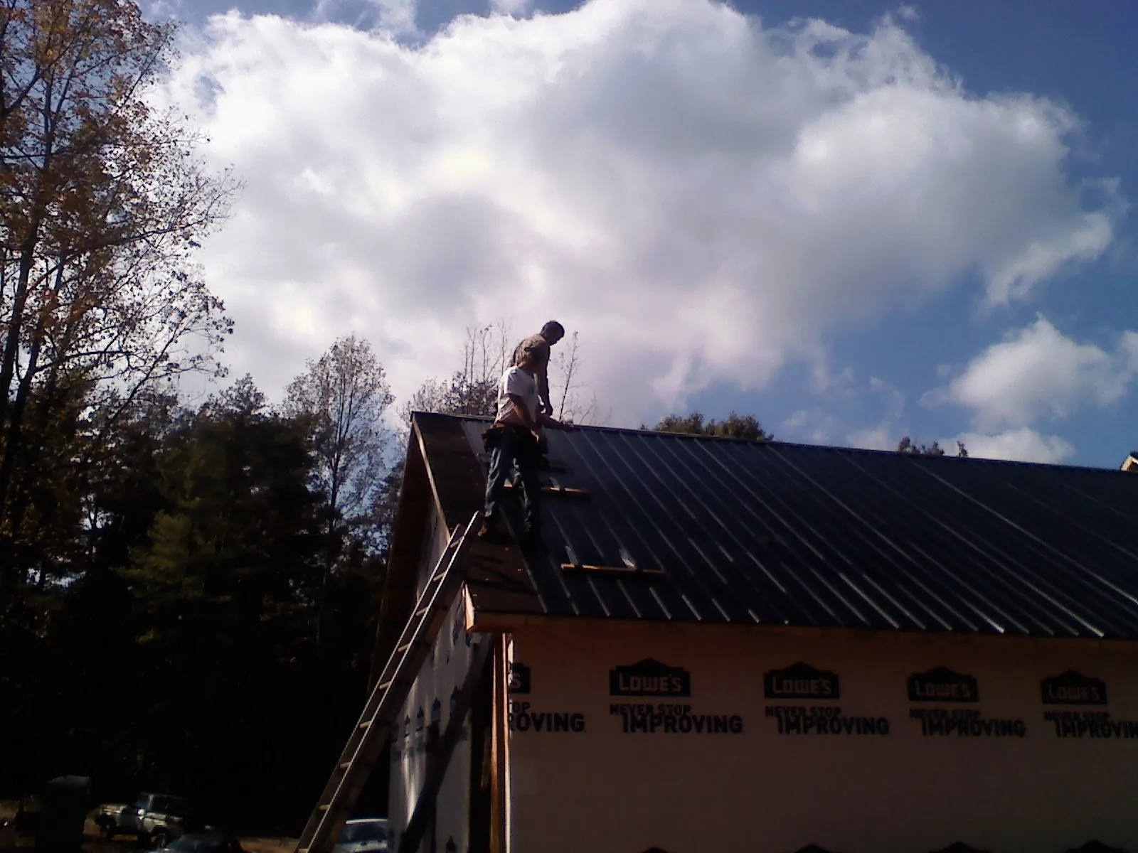 Roofer fastening dark metal panels high against a cloudy sky, from a Roof Inspection job in Corral