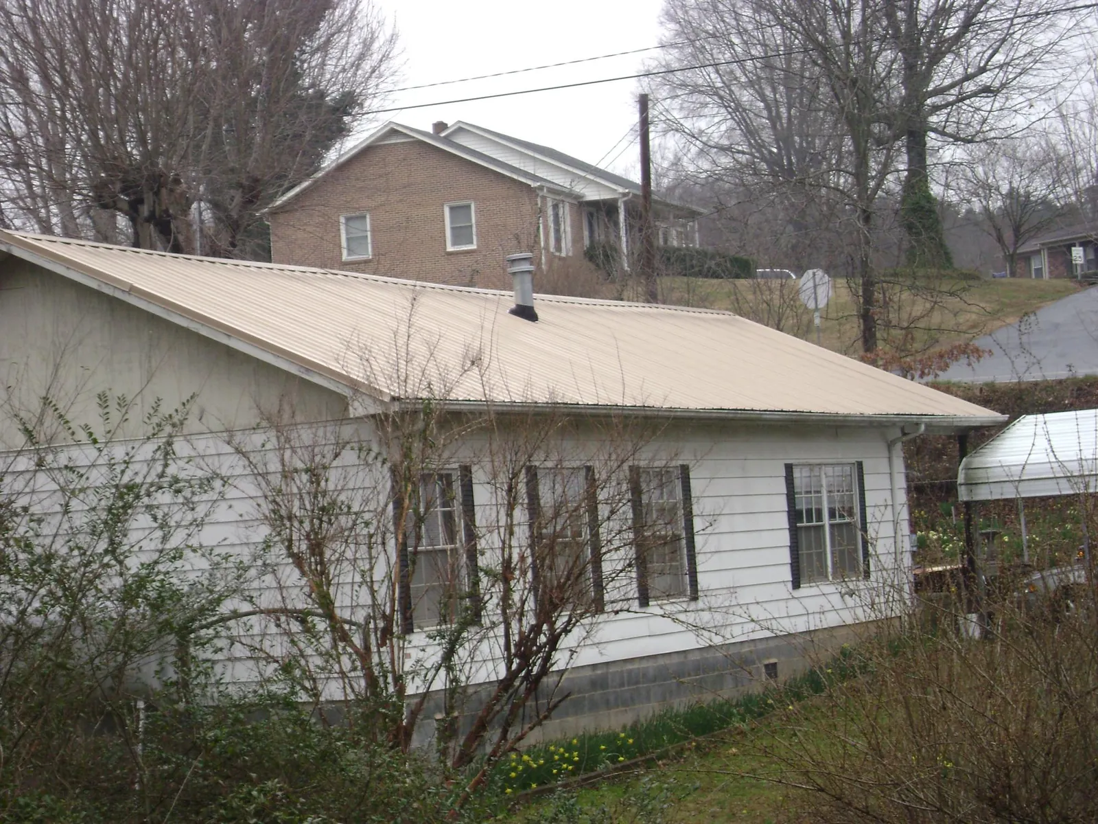 Tan metal roof on a white sided house set into a hillside — Commercial Roofing by Roofing Brothers in Corral